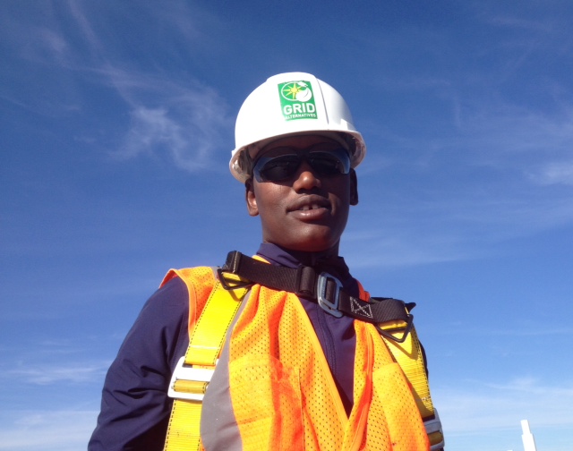 Construction worker wearing GRID hard hat, safety vest, and sunglasses against blue sky