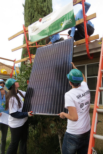 Workers installing a solar panel on a residential roofline during an educational training event