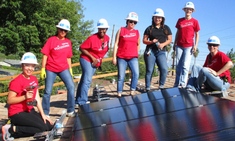 Group of volunteers in red shirts and hard hats installing solar panels on a roof