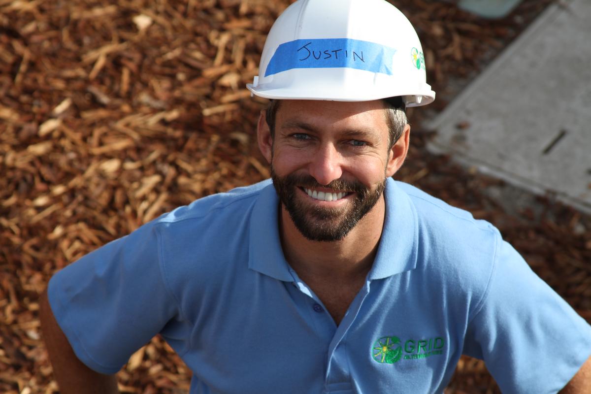 Smiling man named Justin wearing hard hat and blue polo shirt with company logo at construction site