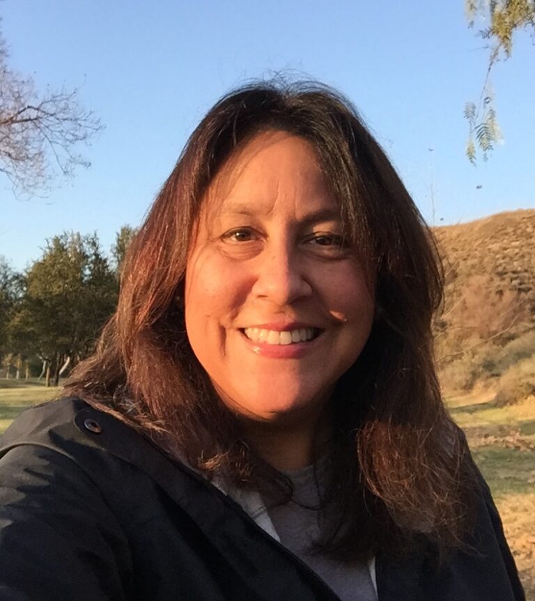 Mary Luévano smiling outdoors with trees and hills in background