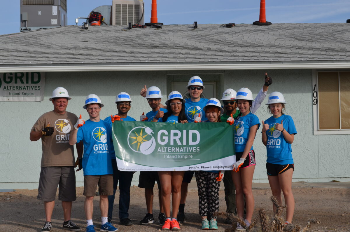 Duke students in hard hats hold GRID Alternatives Inland Empire banner in front of building