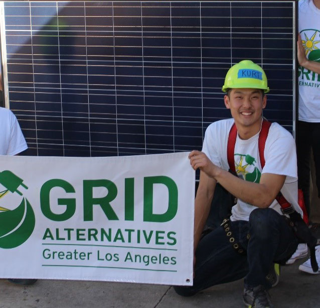 Worker in safety gear holds GRID Alternatives Greater Los Angeles banner in front of solar panel