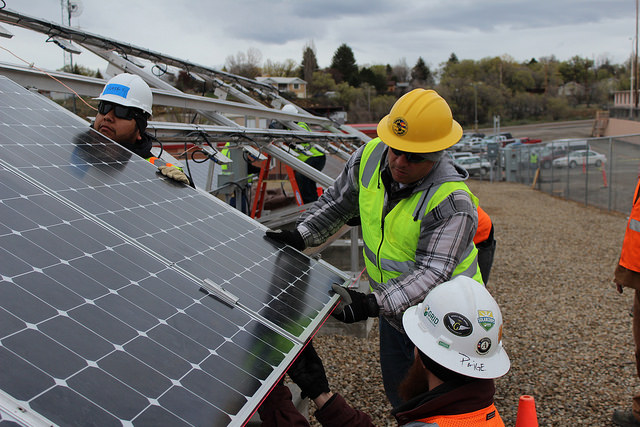 Workers in hard hats install solar panels on a rooftop construction site