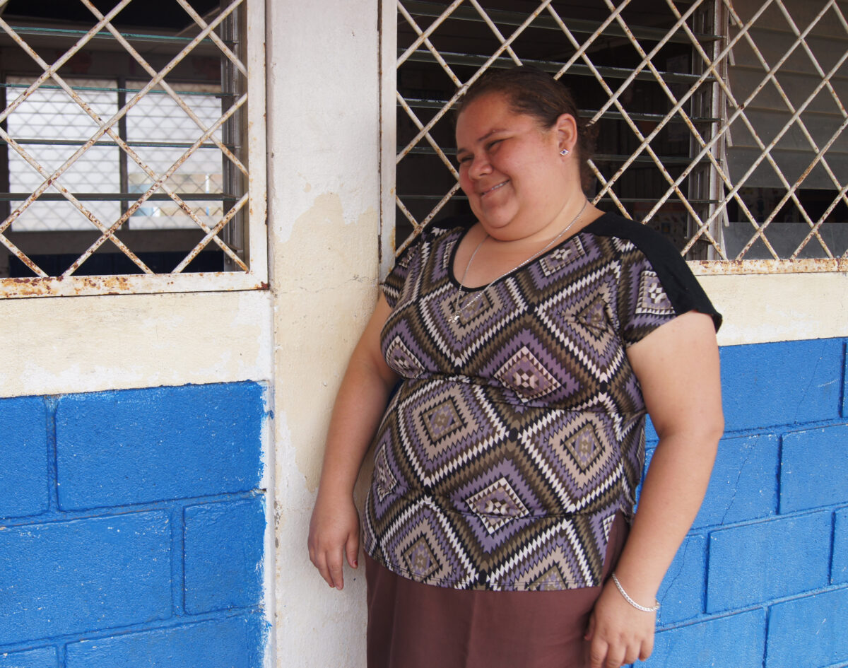 Smiling woman in patterned purple top standing against blue and white building with metal gate windows