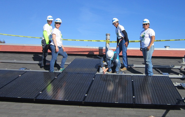 Team of workers installing solar panels on a rooftop under clear blue sky