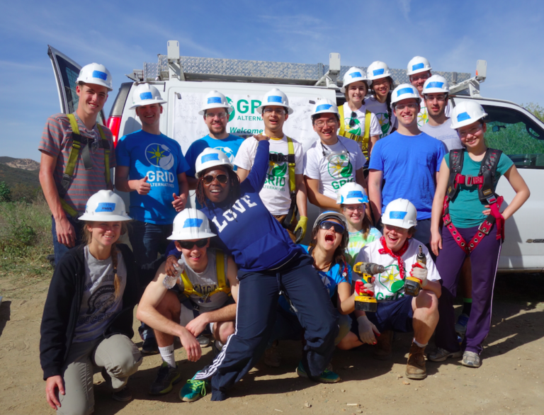 Group of volunteers in hard hats and safety vests posing with GRID Alternatives van for community service project