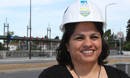 Woman wearing white hard hat smiling at construction site with solar panels in background