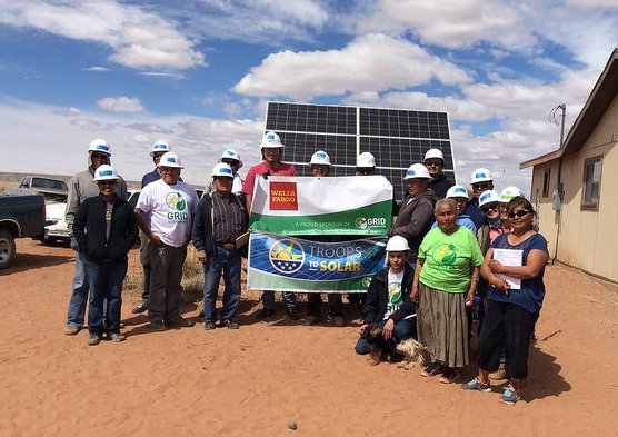 Group holding Navajo solar energy project banner with installed solar panels in background on desert landscape