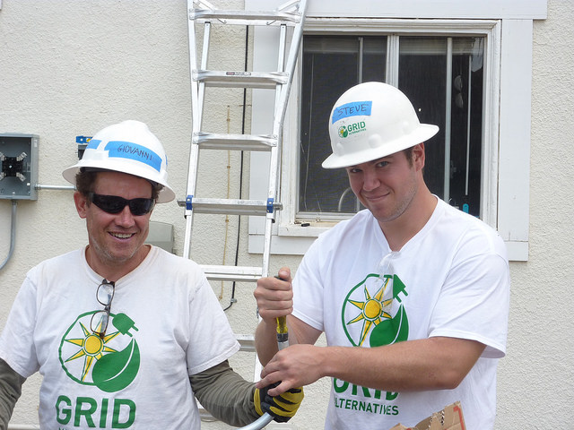 Two men in GRID hard hats and t-shirts hold a hammer during solar construction work training