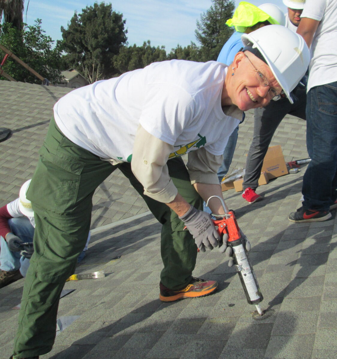 Roofing instructor demonstrating pneumatic nail gun technique to students on residential roof