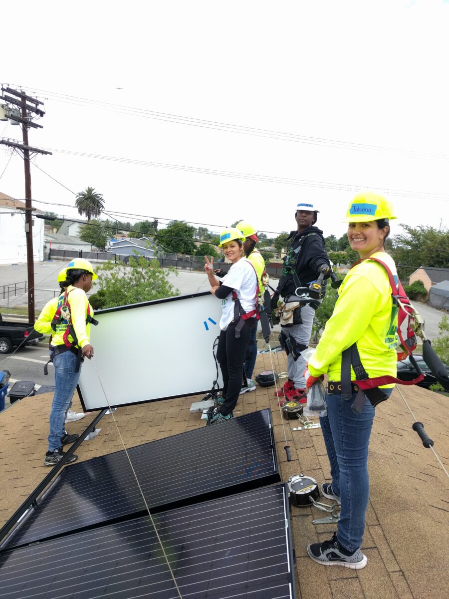 Group of women in safety gear installing solar panels on a rooftop during a training event