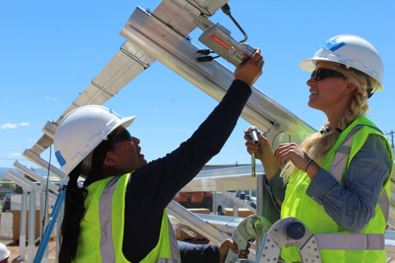 Two construction workers in safety gear inspecting solar panels on a rooftop installation