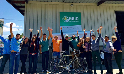 Cross-country cyclist and GRID team members celebrate with raised arms in front of GRID building