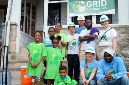 Group of volunteers in green GRID Alternatives shirts posing together outside a building for a community event