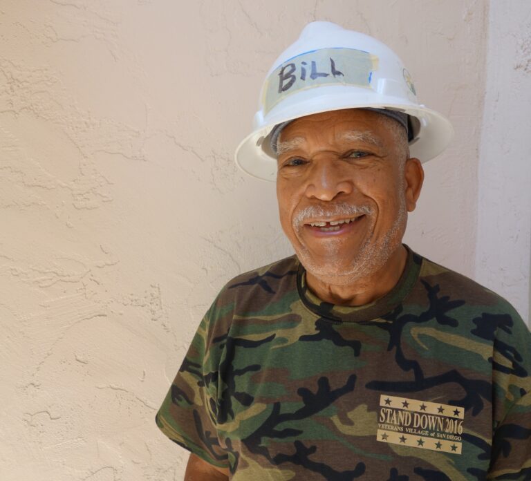 Smiling man wearing white hard hat labeled "BILL" and camouflage shirt reading "Stand Down 2016 Veterans Village San Diego