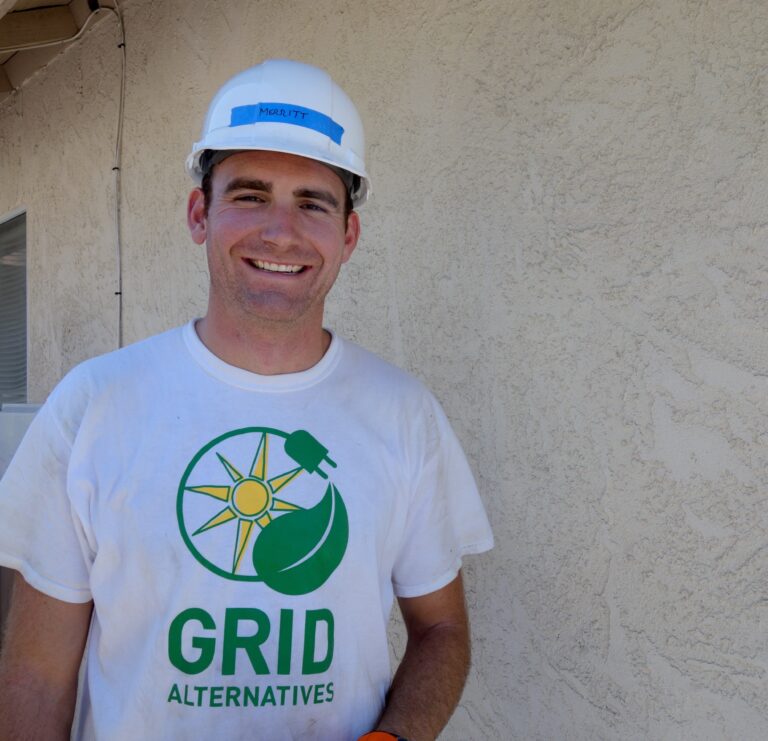 Smiling man wearing GRID Alternatives t-shirt and hard hat labeled Merritt
