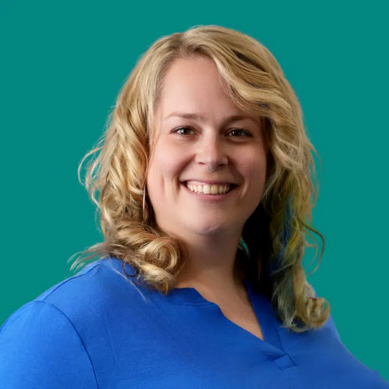 Katie Kerr smiling at camera, wearing blue scrubs against teal background