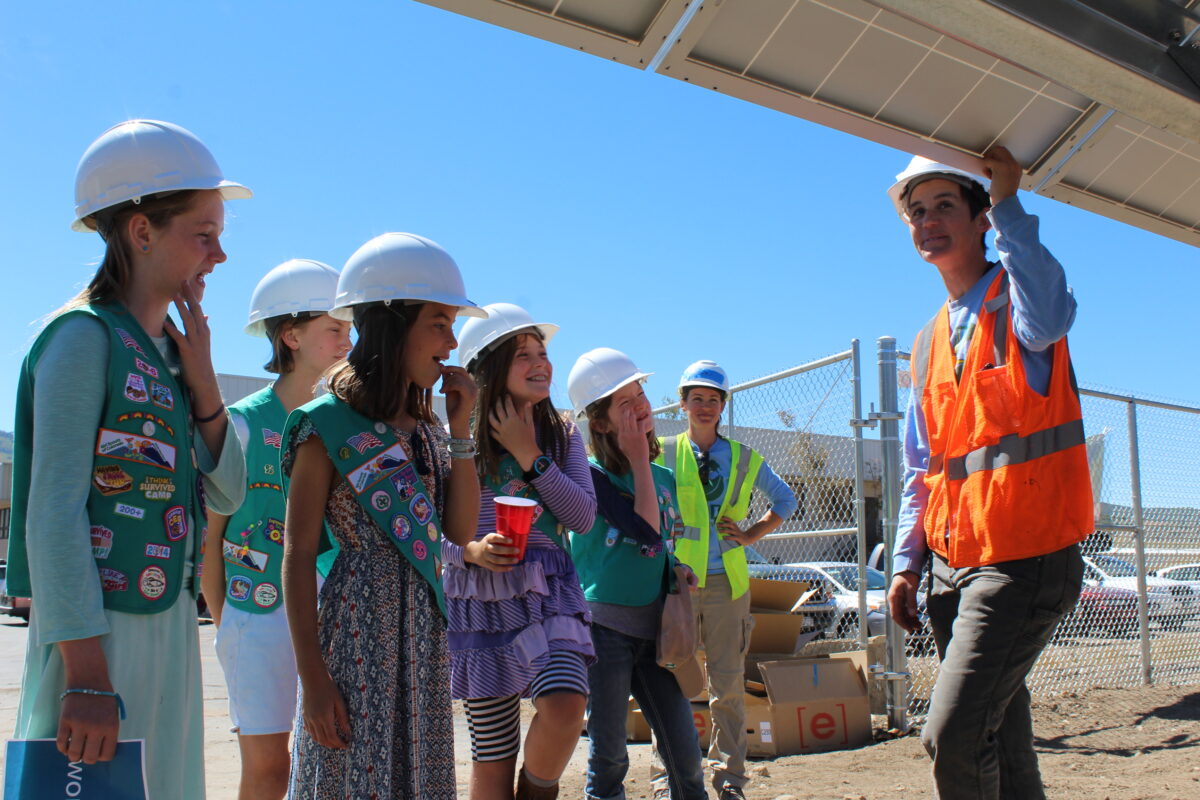 Girl Scout Junior troop members wearing hard hats tour a solar panel construction site with a female instructor