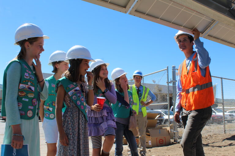 Girl Scout Junior troop members wearing hard hats tour a solar panel construction site with a female instructor