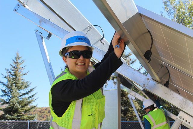 Worker in safety gear installing solar panel on residential structure