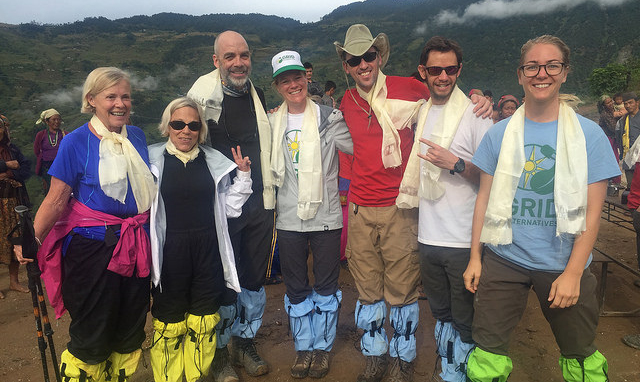 Group of hikers posing together on a mountain trail with misty green peaks in the background
