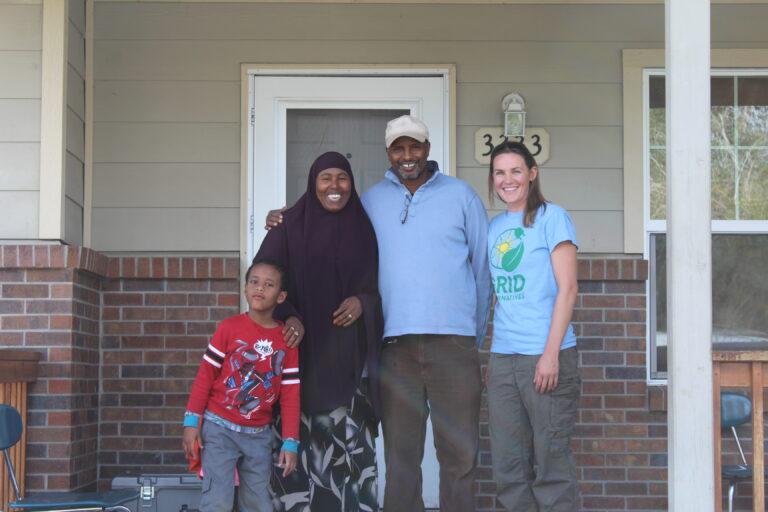 Four people smiling on a residential porch with house number 333 visible behind them