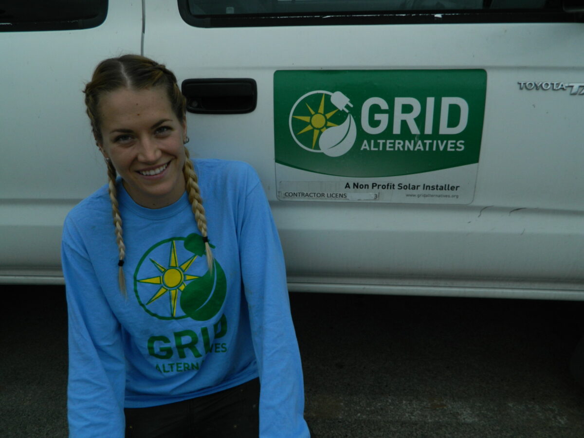 Woman in GRID Alternatives shirt smiling in front of white van with company logo and "A Non Profit Solar Installer" text