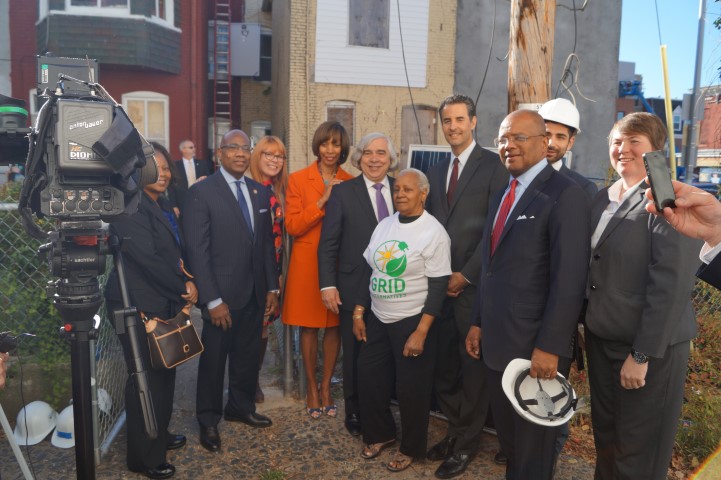 Group of officials and dignitaries at solar panel installation event with "GRID" signage visible