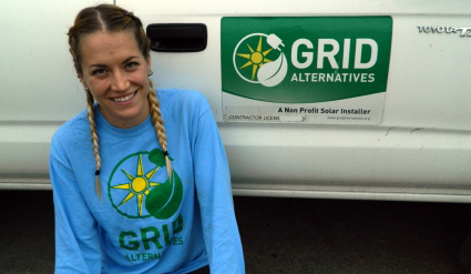 Woman in blue Grid Alternatives shirt smiling next to solar installation vehicle