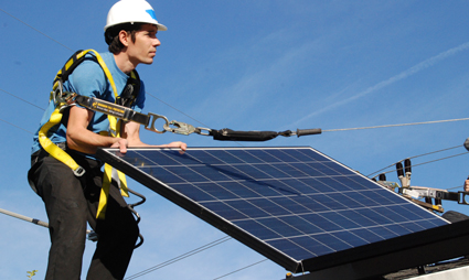 Worker in safety harness installing solar panel on rooftop