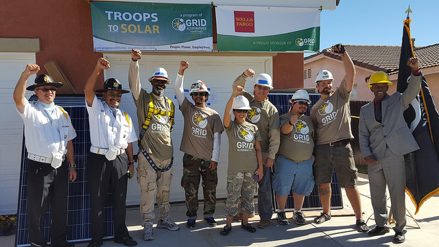 Group of people in hard hats and work vests raising joined hands in celebration at a "Troops to Solar" GRID event