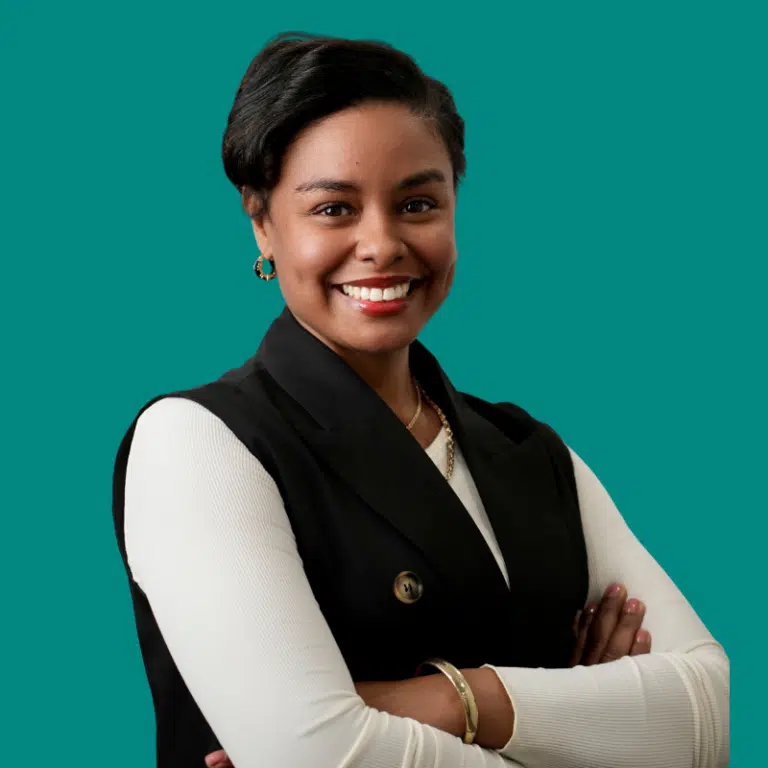Professional headshot of Antia Smith smiling against a teal background, wearing a black vest over white top
