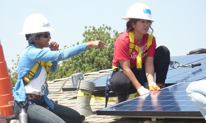 Two workers installing solar panels on a rooftop, wearing hard hats and safety gear
