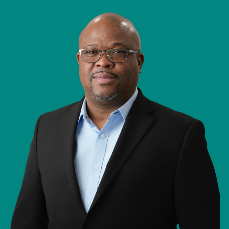 Professional headshot of Adewale OgunBadejo against teal background, wearing black blazer and light blue shirt with glasses