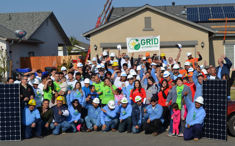 Large group of GRID Alternatives workers and volunteers in hard hats celebrate solar installation success in the Central Valley