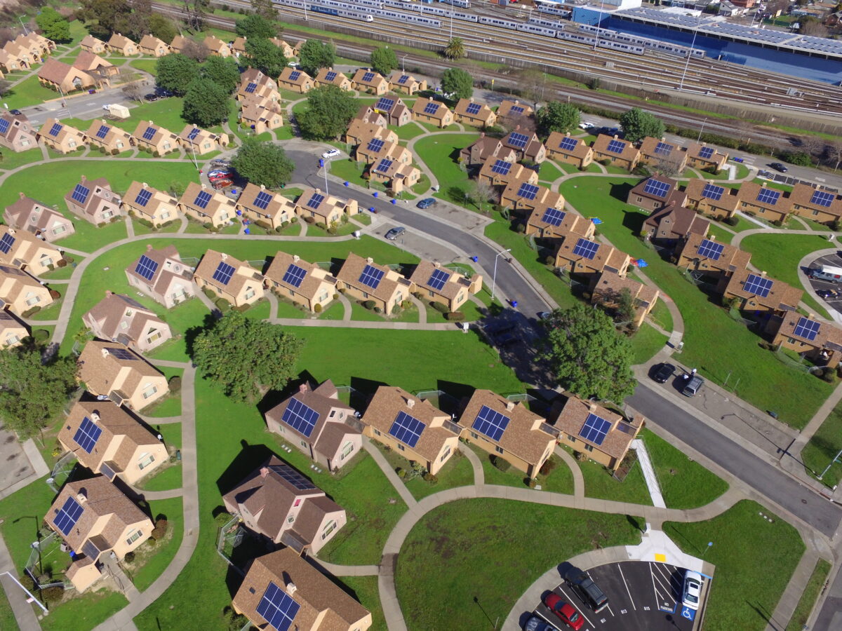 Aerial view of residential neighborhood with solar panels on rooftops of brick houses arranged along curved streets near railway tracks