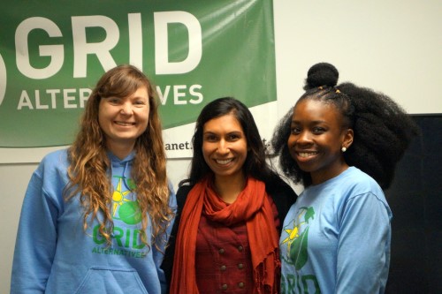 Three young women smiling at camera in front of green "Grid Alternatives" banner