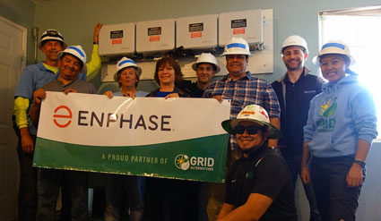 Team of workers in hard hats holding Enphase banner at solar installation site