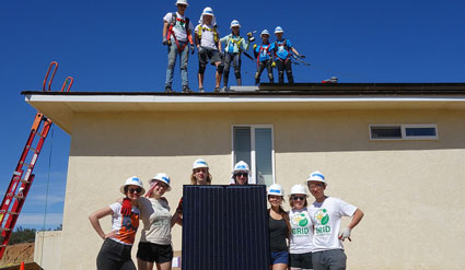 Construction workers in hard hats pose on and in front of a residential building with solar panels during Solar Spring Break 2017