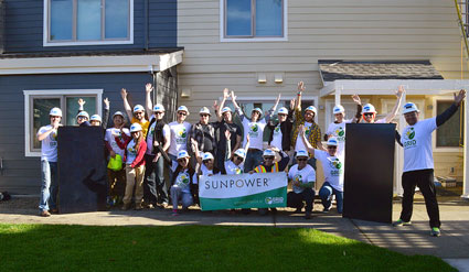 SunPower volunteers celebrate together in front of a house, holding a green banner that reads "SunPower
