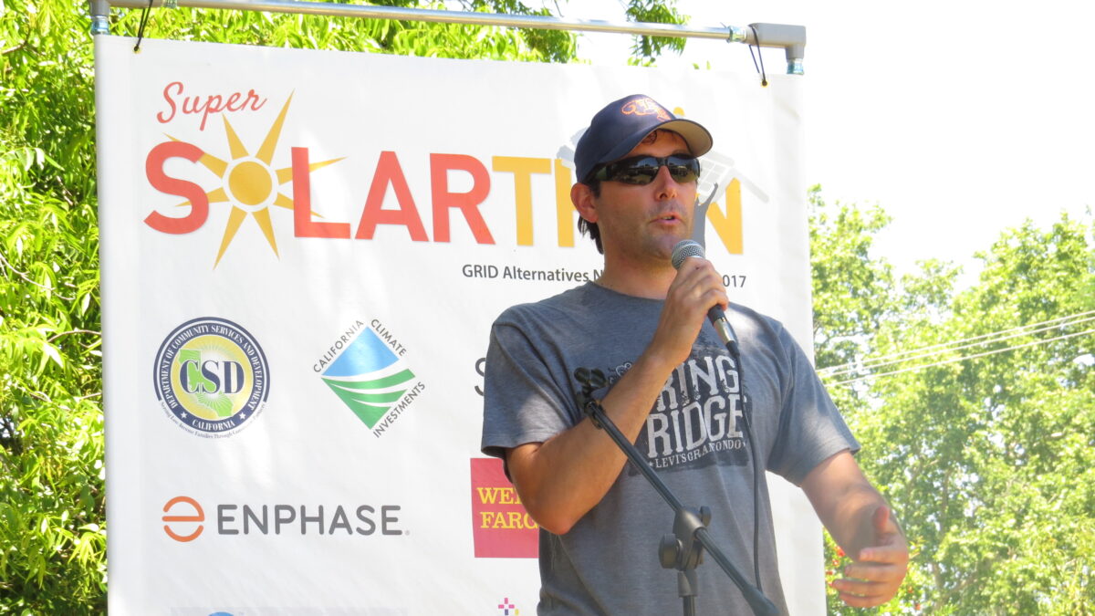 Man speaking at microphone in front of Super Solarthon banner with sponsor logos