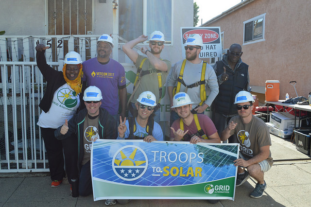 Group of service members wearing hard hats holding "Troops to Solar" banner at construction site