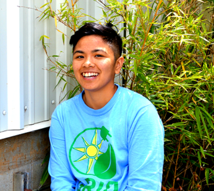 Smiling young man in light blue shirt with sun and leaf graphic, outdoors by bamboo plants