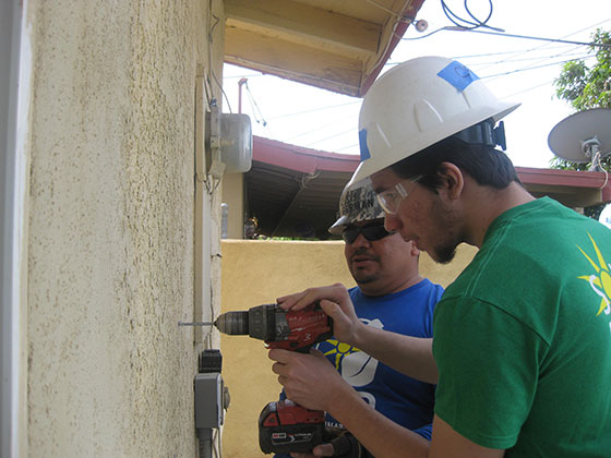 Two workers installing solar equipment on a residential building wall