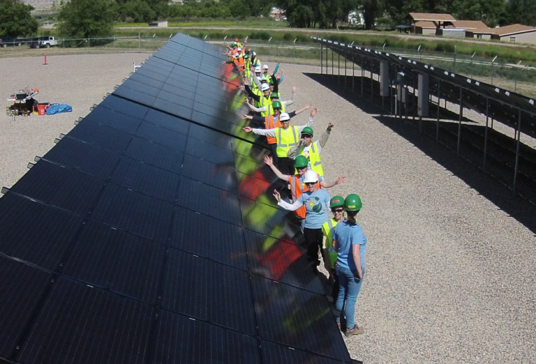 Group of workers in safety gear installing large solar panel array at outdoor facility