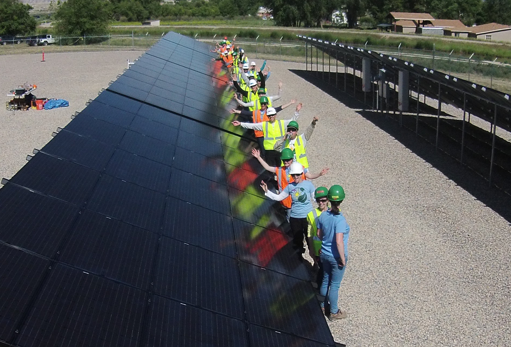 Group of workers in safety gear installing large solar panel array at outdoor facility