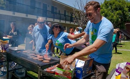 Man grilling food at outdoor community event with residents gathered around