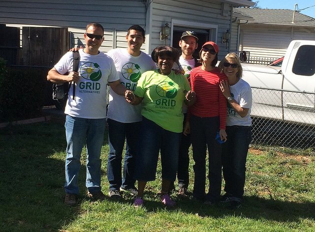 Six volunteers in GRID t-shirts pose together on a sunny residential lawn during a Solarthon event