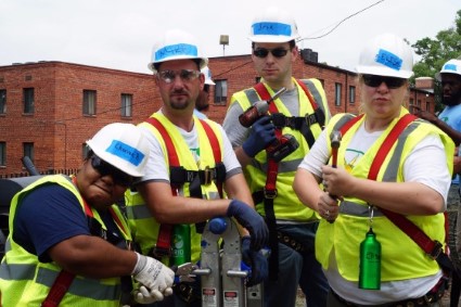 Construction workers in safety gear and hard hats examining equipment outdoors near a brick building